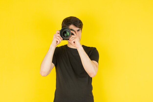 Retrato de un joven tomando fotos con cámara contra amarillo.