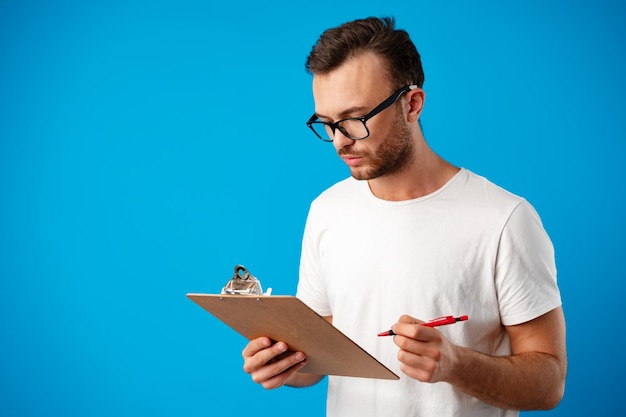 Retrato de joven tomando notas en el portapapeles contra el fondo azul.