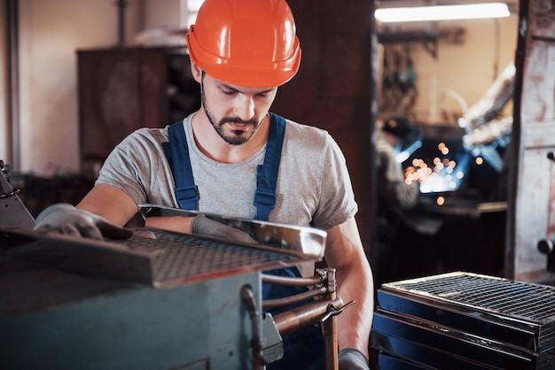 Retrato de un joven trabajador con un casco en una gran planta metalúrgica.