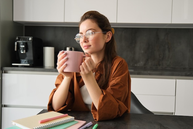 Foto gratuita retrato de una joven trabajadora independiente que trabaja desde casa tomando un descanso para tomar un café sentada con