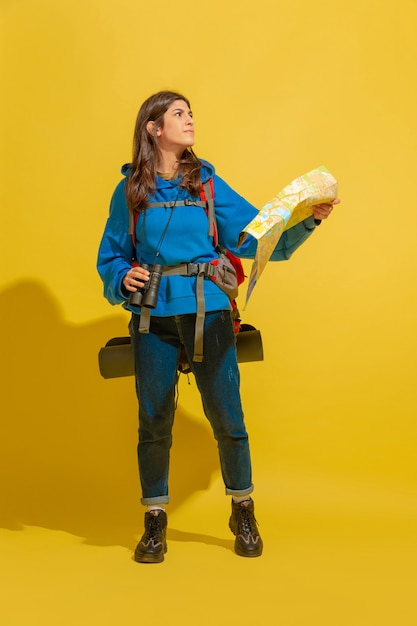 Foto gratuita retrato de una joven turista alegre con bolsa y binoculares aislado en la pared amarilla del estudio