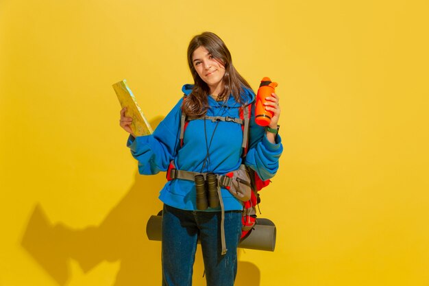 Retrato de una joven turista alegre con bolsa y binoculares aislado en la pared amarilla del estudio