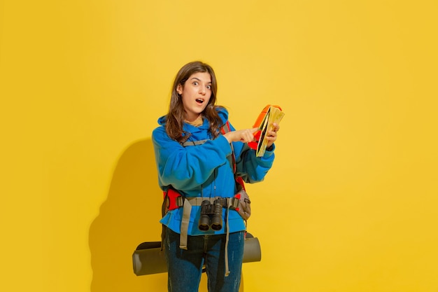 Retrato de una joven turista alegre con bolsa y binoculares aislado en la pared amarilla del estudio