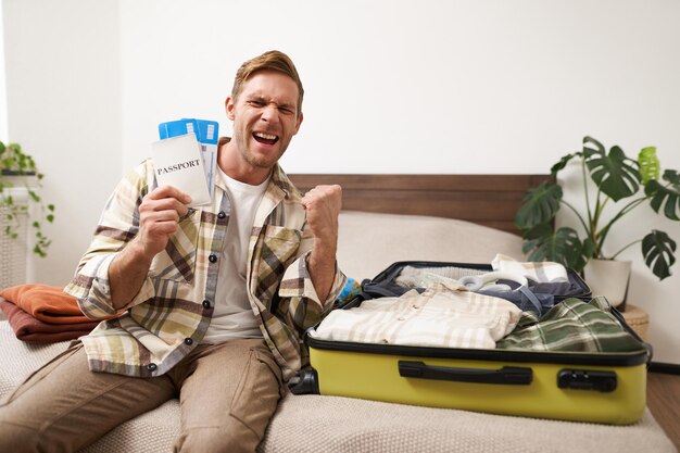 Retrato de un joven turista feliz y emocionado que sostiene su pasaporte y boletos de avión con la ropa envuelta