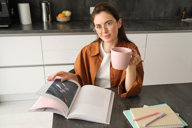 Foto gratuita retrato de una joven tutora preparando una lección para los estudiantes sentados en casa volteando páginas de un libro