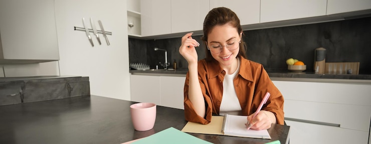 Foto gratuito retrato de una joven tutora sonriente preparando notas para la lección en casa escribiendo en un cuaderno y