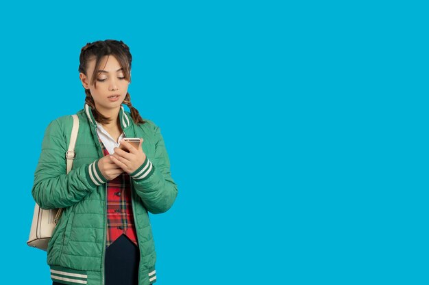 Retrato de una joven universitaria sosteniendo un teléfono y de pie sobre fondo azul. foto de alta calidad