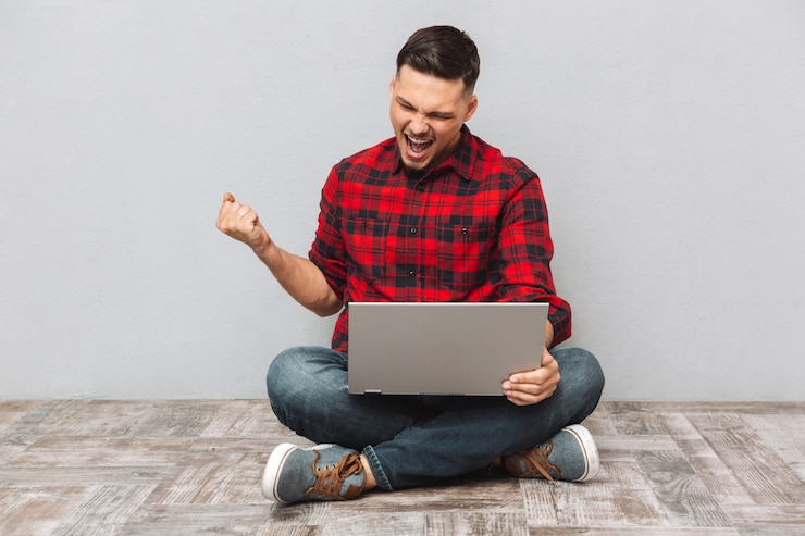 Foto gratuito retrato de un joven usando una computadora portátil y celebrando el éxito