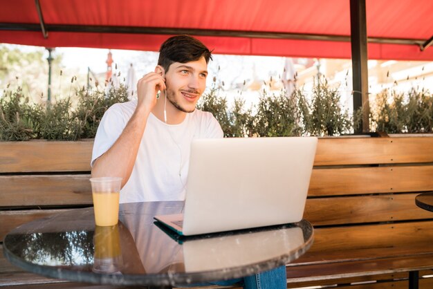 Retrato de joven usando su computadora portátil mientras está sentado en una cafetería. Concepto de tecnología y estilo de vida.