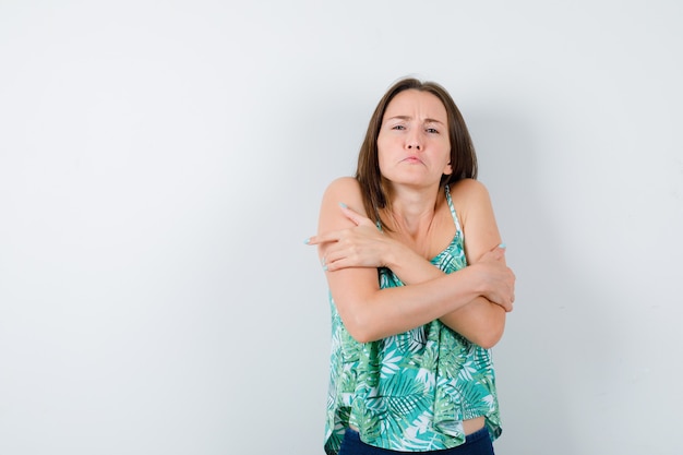 Foto gratuita retrato de jovencita abrazándose a sí misma, sintiendo frío y luciendo sombría vista frontal