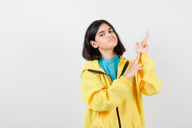 Retrato de jovencita apuntando hacia arriba en chaqueta amarilla y mirando confiado vista frontal