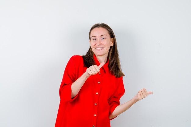 Foto gratuita retrato de jovencita apuntando a la derecha con los pulgares en blusa roja y mirando alegre vista frontal