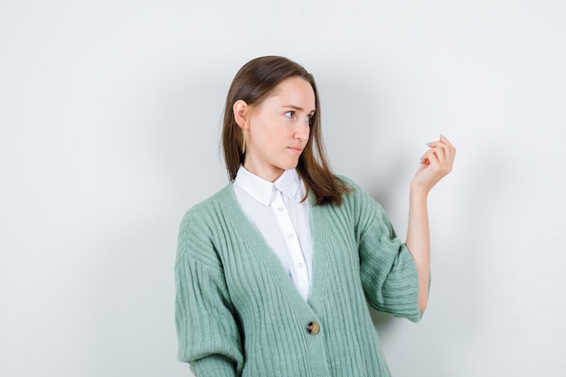 Retrato de jovencita invitando a venir mientras mira a un lado en camisa, cárdigan y mira enfocada vista frontal