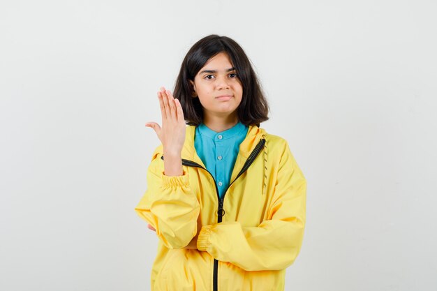 Retrato de jovencita mostrando uñas en camisa, chaqueta amarilla y mirando curiosa vista frontal