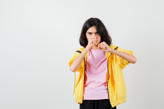 Retrato de jovencita de pie en pose de lucha en camiseta, chaqueta y mirando enfocado vista frontal