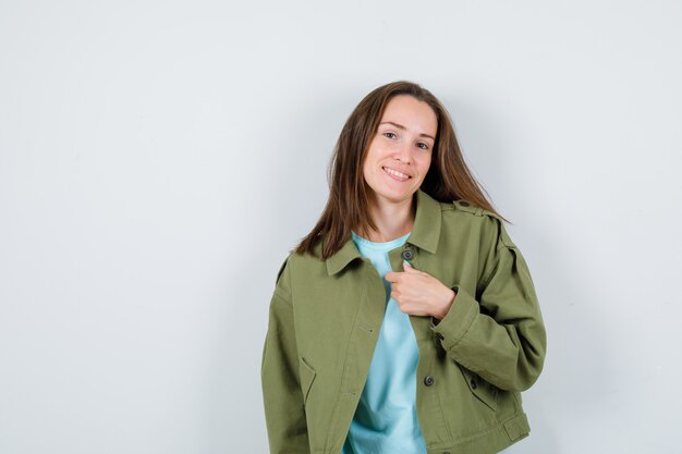 Retrato de jovencita posando mientras está de pie en camiseta, chaqueta y mirando alegre vista frontal