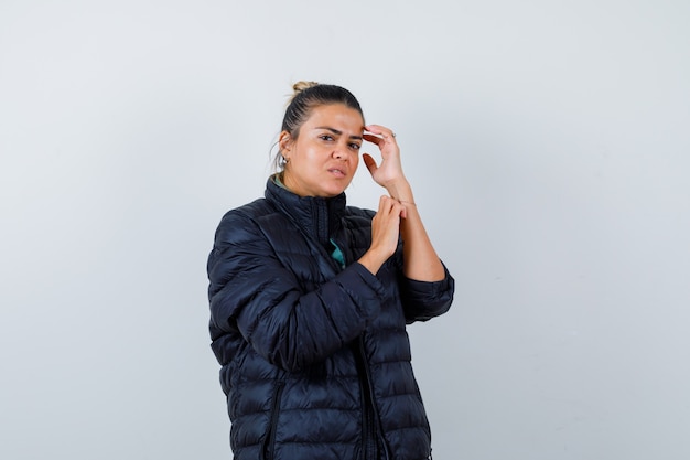 Retrato de jovencita posando mientras toca la cabeza en chaqueta acolchada y mirando elegante vista frontal