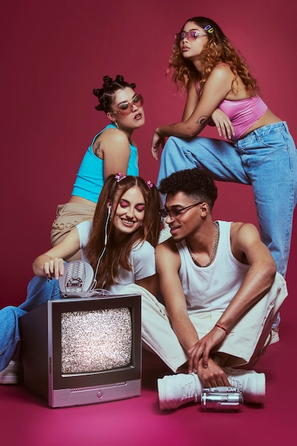 Retrato de jóvenes amigos al estilo de la moda de los años 2000 posando con televisión