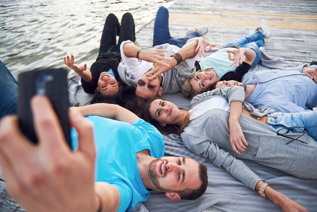 Retrato de jóvenes amigos felices en el muelle en el lago. Mientras disfruta del día y hace selfie.