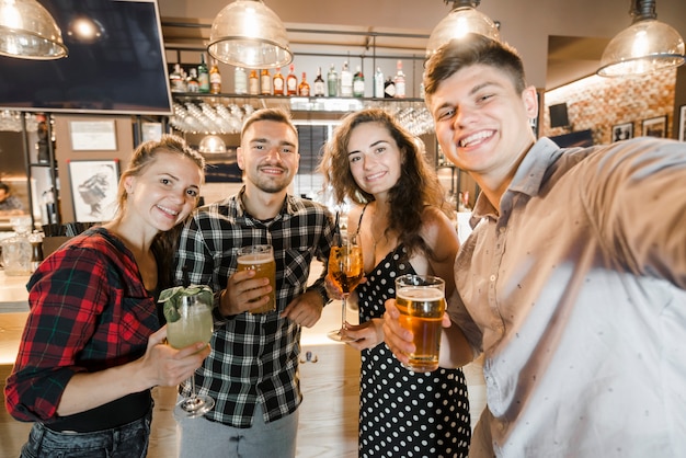 Retrato de jóvenes amigos sosteniendo vasos de bebidas en el bar