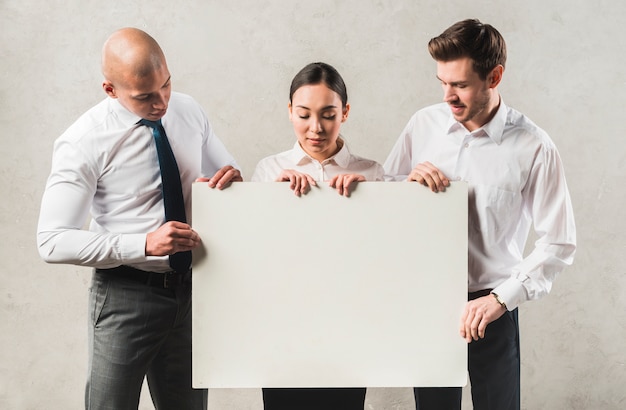 Retrato de jóvenes empresarios mirando gran cartel en blanco de pie contra la pared gris