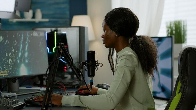 Retrato de jugador africano concentrado mirando a la cámara sonriendo, jugando videojuegos de disparos espaciales en línea para torneos de juegos. Rendimiento cibernético en una PC potente con videojuegos de transmisión de teclado RGB