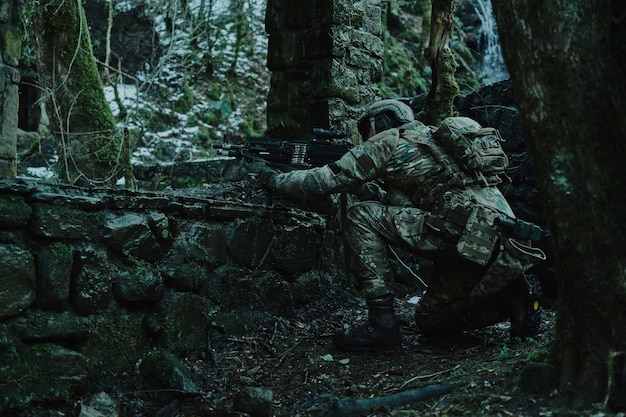 Retrato de jugador de airsoft en equipo profesional en casco apuntando a la víctima con pistola en el bosque. soldado con armas en guerra