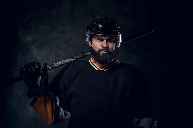 Retrato de un jugador de hockey barbudo serio con su equipo deportivo en las manos.