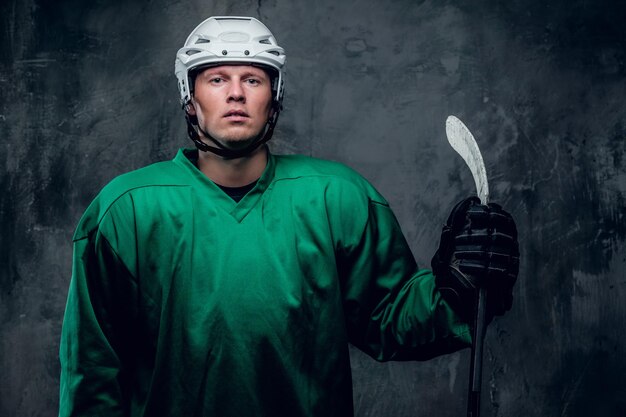 Retrato de un jugador de hockey con ropa protectora sostiene un palo de juego sobre fondo gris.