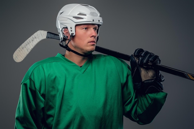 Retrato de jugador de hockey sostiene palo de hielo aislado sobre fondo gris.