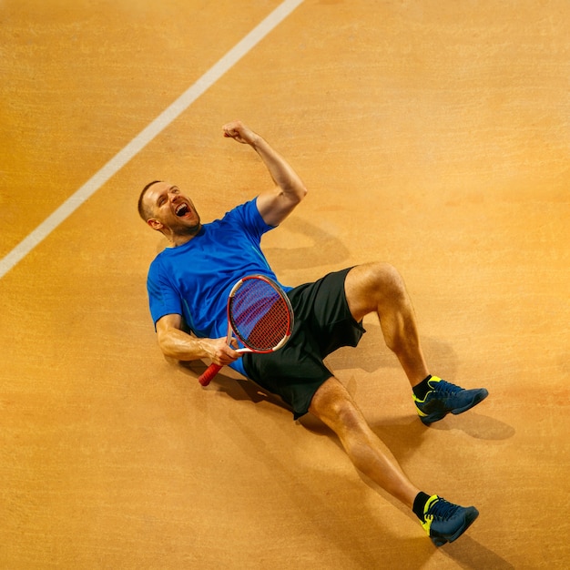 Retrato de un jugador de tenis masculino guapo celebrando su éxito en una pared de la cancha. Las emociones humanas, ganador, deporte, concepto de victoria