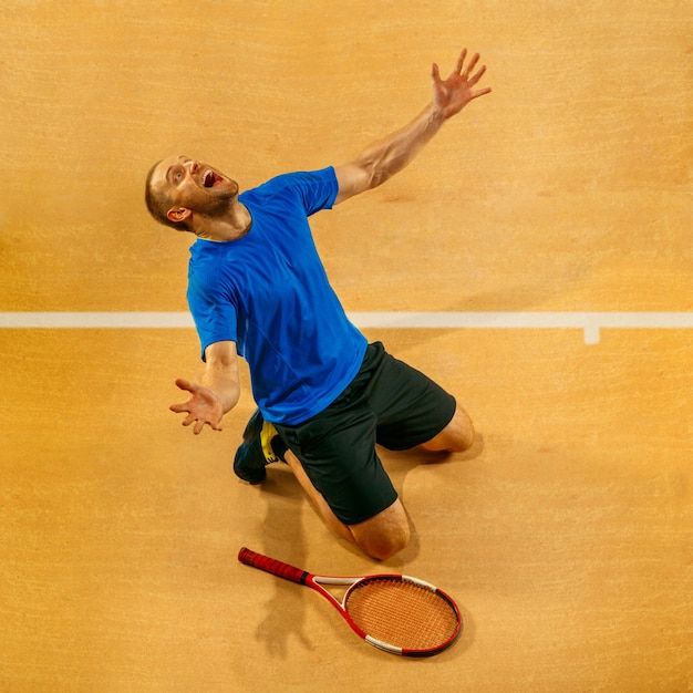 Retrato de un jugador de tenis masculino guapo celebrando su éxito en una pared de la cancha. Las emociones humanas, ganador, deporte, concepto de victoria