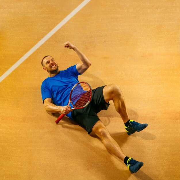 Retrato de un jugador de tenis masculino guapo celebrando su éxito en una pared de la cancha