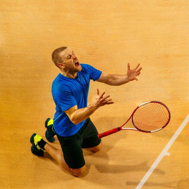 Retrato de un jugador de tenis masculino guapo celebrando su éxito en una pared de la cancha