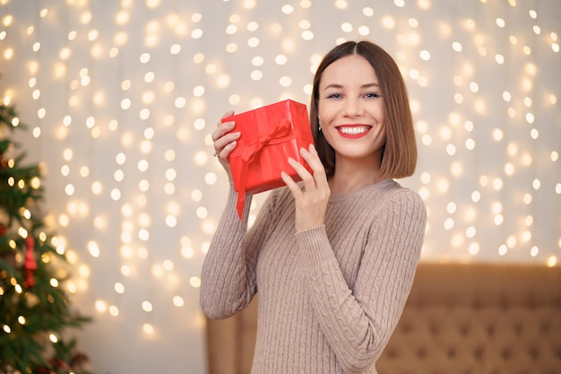 Retrato de labios rojos de joven feliz mirando caja de regalo envuelta.