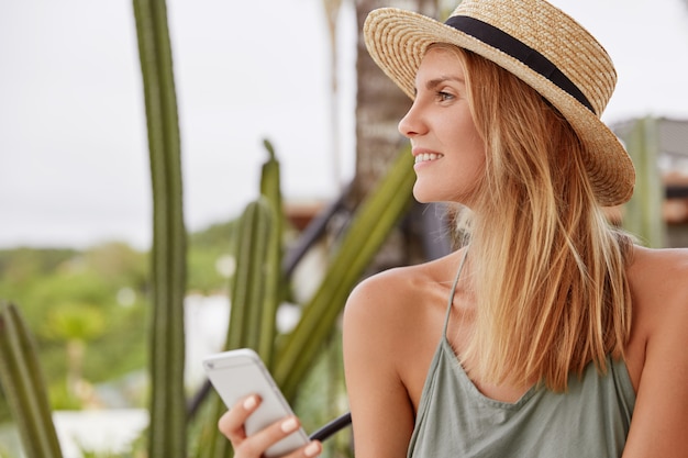 Retrato de lado de mujer encantadora feliz con mirada positiva de ensueño, lleva sombrero de verano