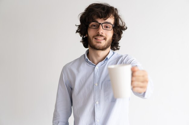 Retrato de las lentes que llevan felices del hombre joven que sostienen la taza.