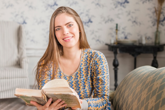 Retrato de un libro de explotación joven sonriente en la mano mirando a cámara