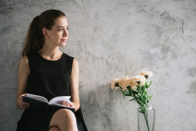 Retrato de un libro de lectura hermoso de la mujer joven que se relaja en sala de estar. Imágenes de estilo de efecto vintage.