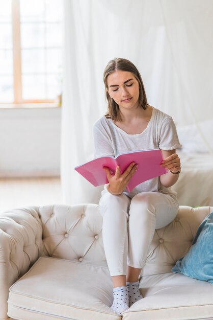 Retrato del libro de lectura de la mujer joven en casa