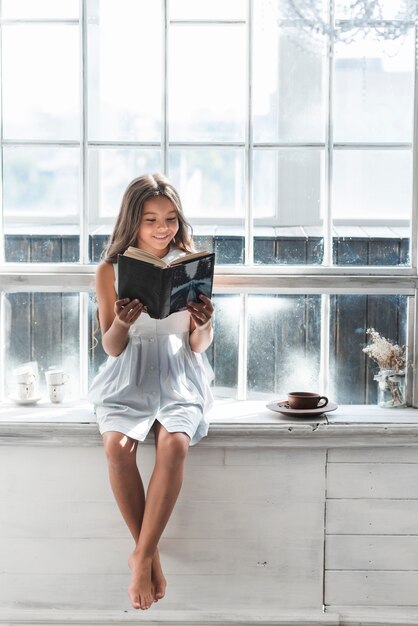 Retrato de un libro de lectura sonriente de la muchacha en casa