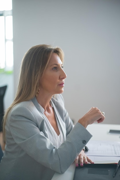 Retrato de una líder empresarial que trabaja en el cargo. Mujer de pelo rubio con traje sentada en la mesa analizando datos financieros pensando en nuevos proyectos mirando a un lado. Concepto de inicio y crecimiento empresarial