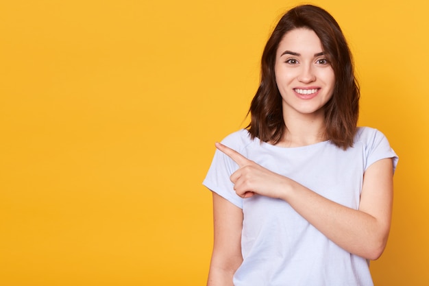 Retrato de linda chica alegre encantadora apuntando a un lado con el dedo índice