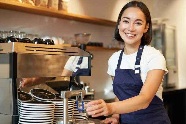 Foto gratuita retrato de una linda chica barista que trabaja detrás del mostrador haciendo café con leche humeante para usar capuchino