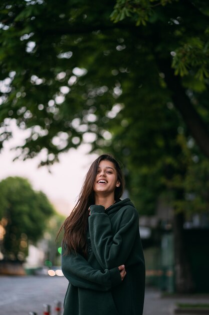 Retrato de linda chica con cabello largo mira a la cámara en la ciudad en la calle