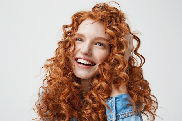 Foto gratuita retrato de linda chica feliz sonriendo tocando su pelo rojo rizado.