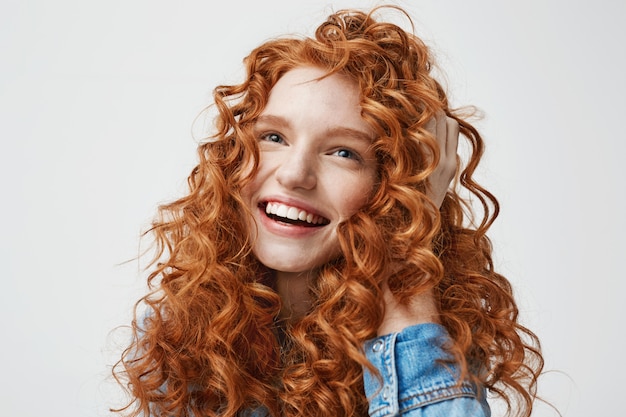 Retrato de linda chica feliz sonriendo tocando su pelo rojo rizado.