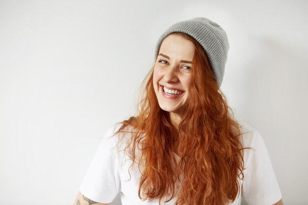 Retrato de linda chica pelirroja con gorra de invierno gris y camiseta blanca sonriendo