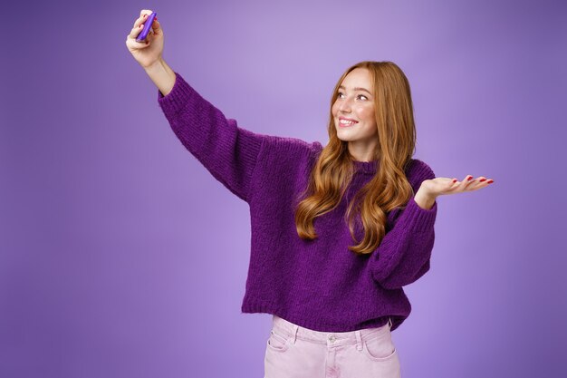 Retrato de linda chica pelirroja de vacaciones tomando selfies cerca de turismo levantando la mano como si estuviera sosteniendo ...