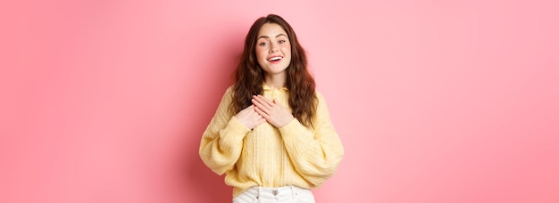 Retrato de una linda chica sincera que aprecia un buen gesto alabado tomados de la mano en el corazón y sig